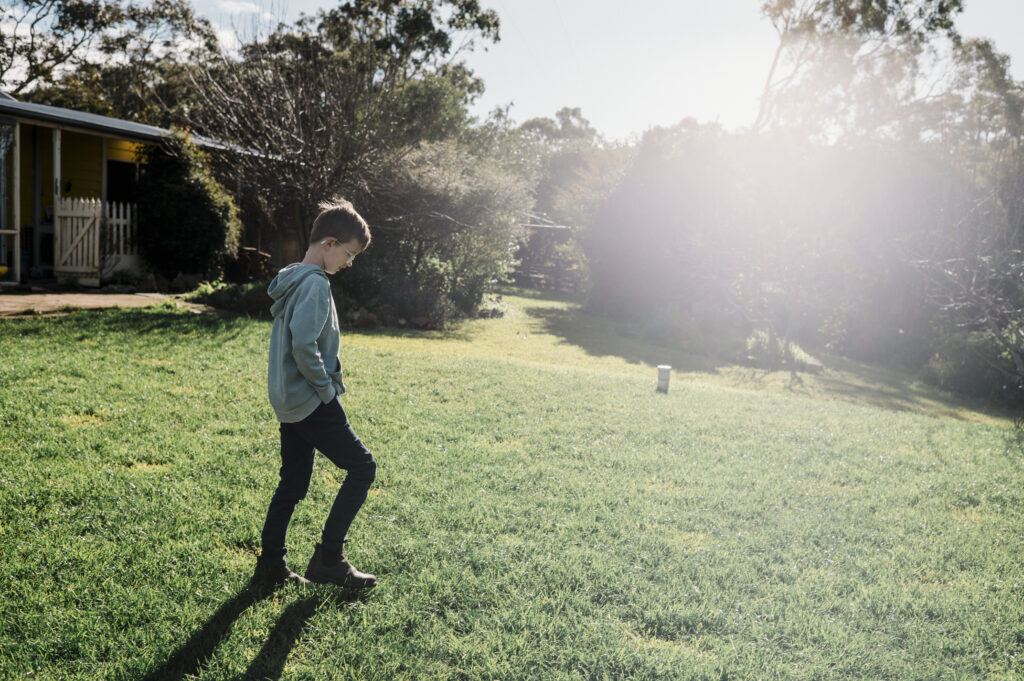 Boy walking in the sunshine across a lawn