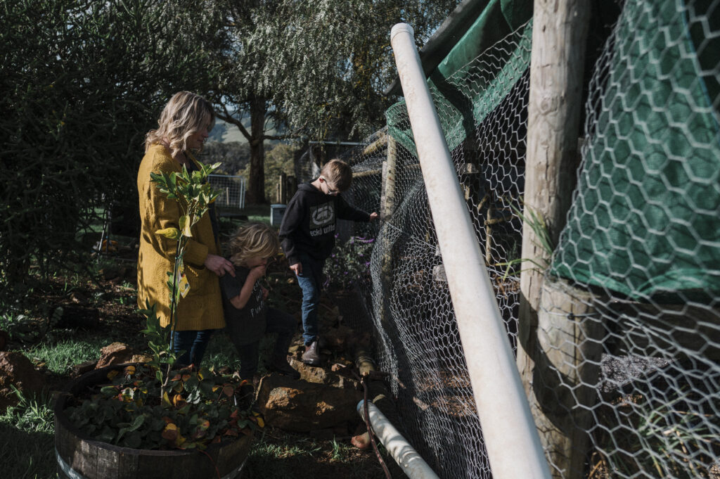 Mother and two sons standing in a garden outside a chicken coop