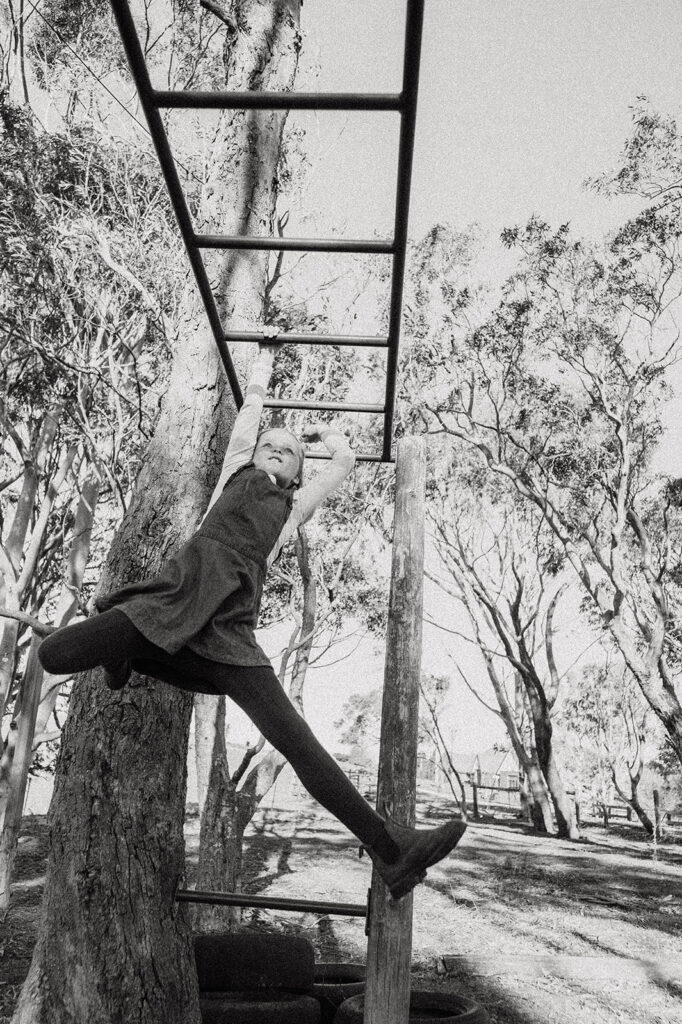 Black and white photo of girl swinging from monkey bars